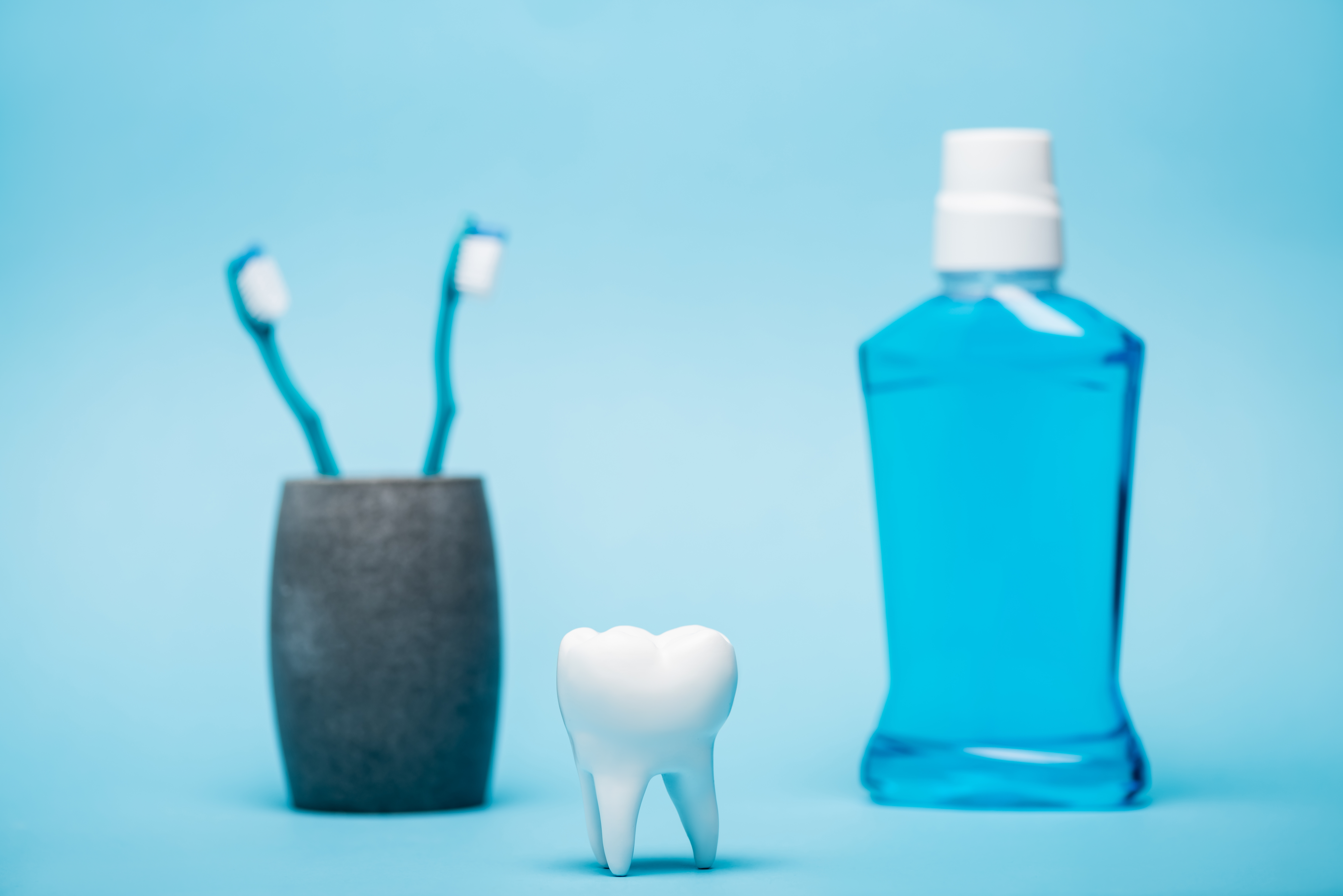 model of tooth near toothbrushes and mouthwash on blurred background on blue background